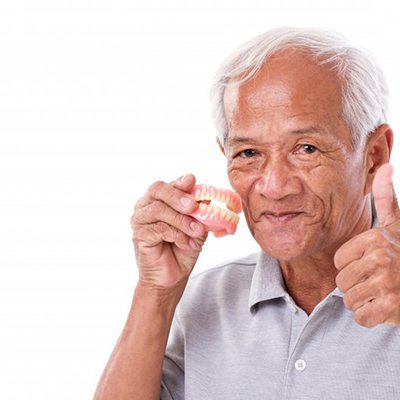 Someone holding dentures and giving a thumbs up