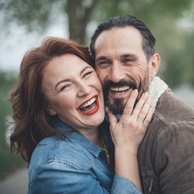 Man and woman sharing healthy smiles after dental implant tooth replacement
